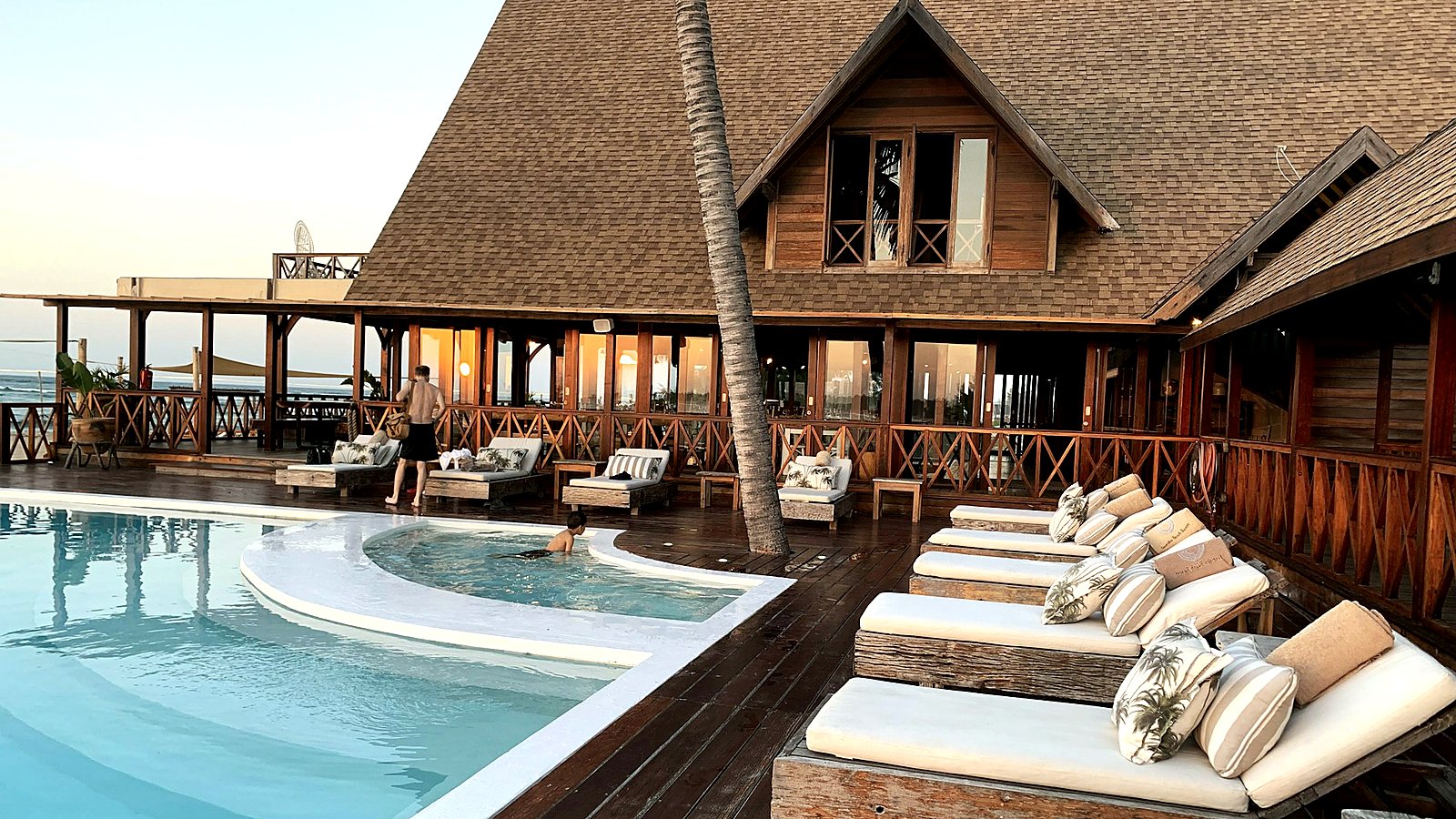 Luxury resort pool deck at dusk with lounge chairs and a wooden clubhouse