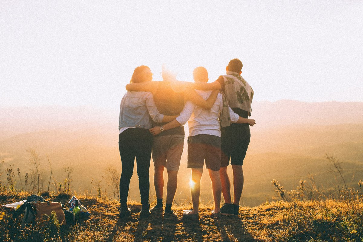 Friends with arms around each other overlooking a sunset landscape after a shared outing