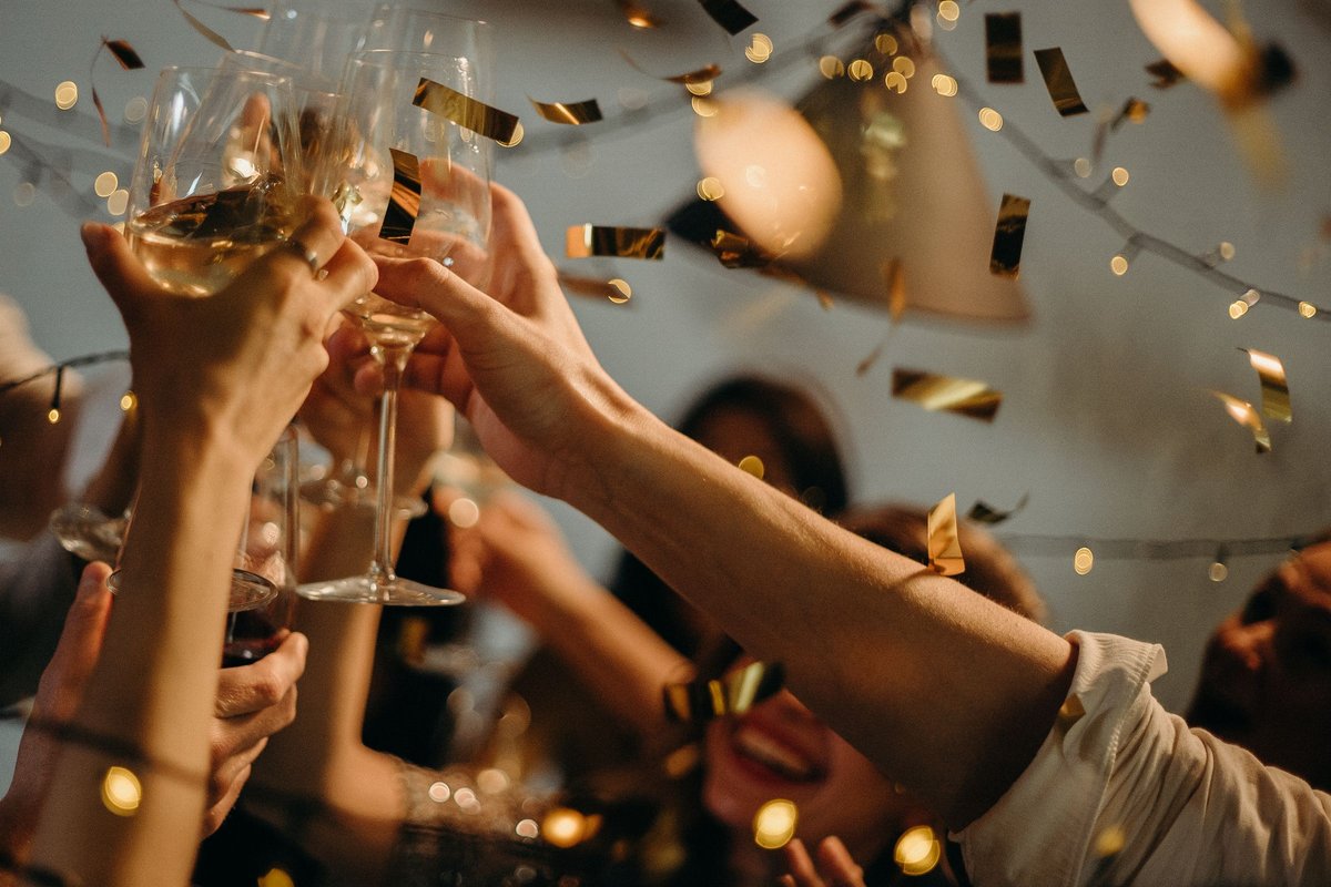 Friends toasting champagne glasses amid gold confetti and warm string lights