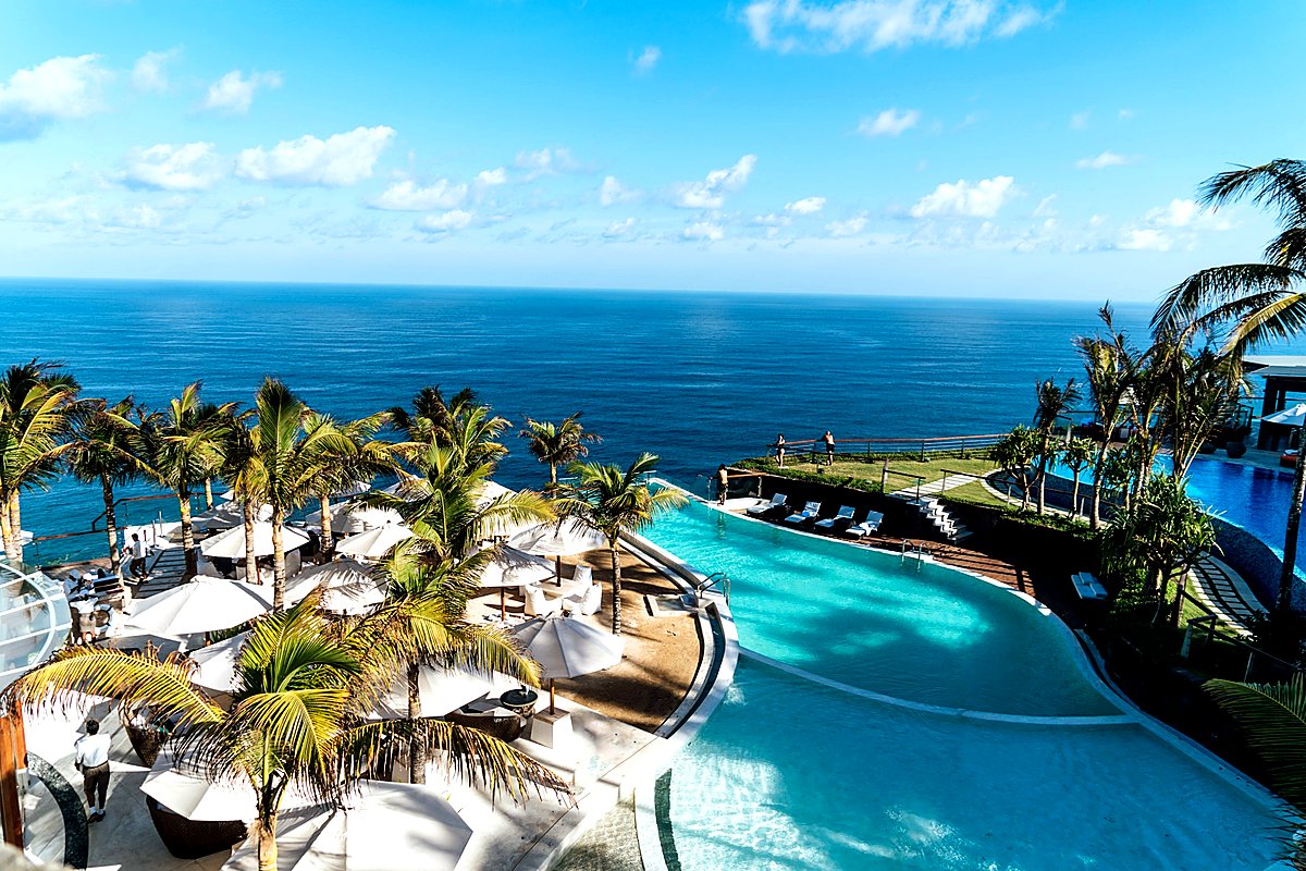Cliffside tropical resort with infinity pools, palm trees, and white umbrellas overlooking the ocean