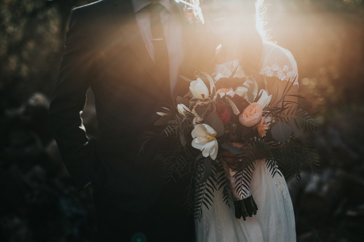 Bride and groom in golden-hour light with a lush wedding bouquet